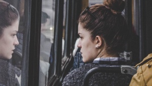 A young woman riding a bus and looking out the window.