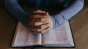 A woman praying with her hands on a Bible.