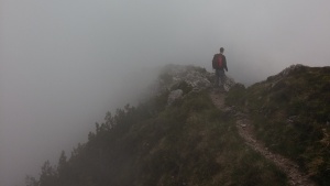 A person hiking on a narrow mountain path surrounded by fog.