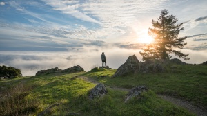 A man standing on top of hill with the sun in the background.