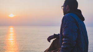 A man sitting by a body of water looking at the sunset.