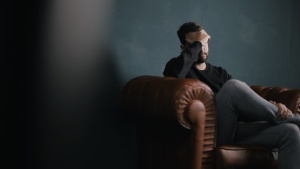 A man sitting on a chair holding his head with his hand.