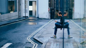 A man sitting by a building looking at his phone.