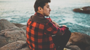 A young man sitting on a rock looking out over the water.