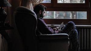 A man sitting in a big chair by a window reading.