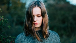 A young woman holding her head down facing the ground.