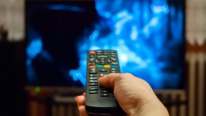 A woman's hand pointing a TV remote control at a television.