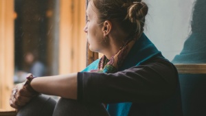 A woman sitting by a large window looking outside.