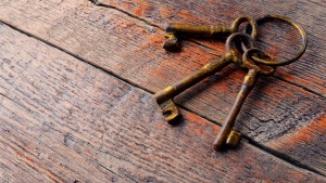 Three old skeleton keys laying on an old wood table.