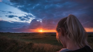 A woman in a field with the sun setting in the distance.