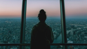 A woman looking outside of window of tall building.