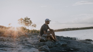 A man sitting on a log by a lake. 