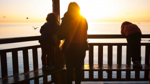 A mom with children on a deck looking over water.