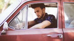 A young man sitting in the driver's seat of an old car.