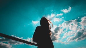 The silhouette of a young woman with the sky and sun in the background.