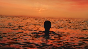 A person floating in the water with the sun setting.