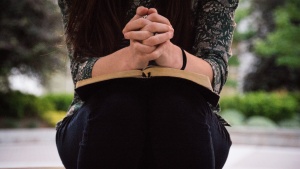 A woman with her clasped in prayer on top of an open Bible.