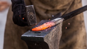 Close-up photo of a hammer striking a heated piece of metal.