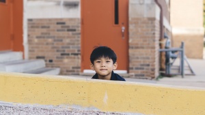 A little boy hiding behind a yellow wall.