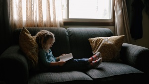 A little girl sitting on a couch looking at a Bible.