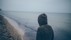 A person walking on a beach wearing a hoodie.