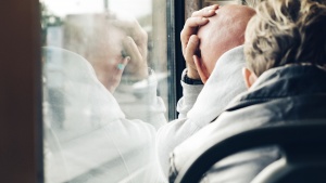 A man leaning his head against a train window.