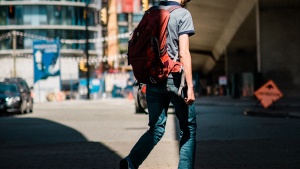 A man writing on the street wearing a backpack.