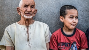 An old man (maybe the grandfather) and young boy sitting against a wall.
