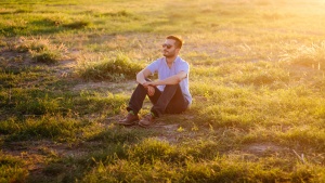 A man sitting in a field with the sun rays shinning.