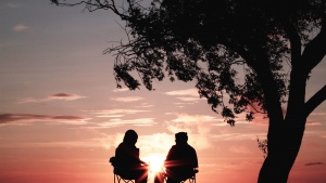 Two people sitting together talking as the sun is setting in the background.