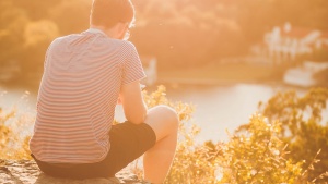 A young man sitting on a rock looking out over the water.