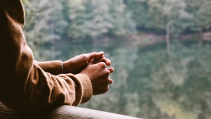 A person resting their arms on rail while looking out over a body of water.