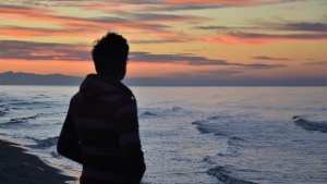 A man looking at a sunset over a body of water.