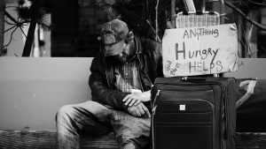A homeless man sitting beside the road with a sign asking for help.