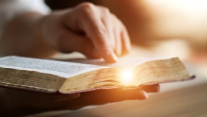 An open Bible with someone's hand pointing to a scripture.