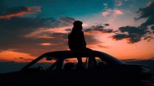 A young man sitting on the top of a car watching the sunset.