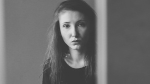 A young woman looking from behind an edge of a wall.