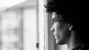 A young man with dark hair staring out a window.