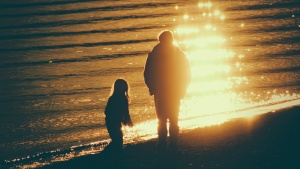 A dad and his children walking on the beach as the sun is setting.