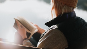 A woman sitting by a lake paging through a Bible.