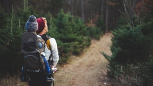 A woman hiking on a trail with a child on her back.