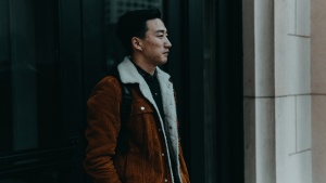 A man walking on sidewalk next to an old building.