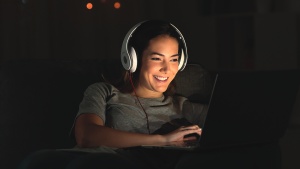 A girl wearing headphones while watching the screen of a laptop.