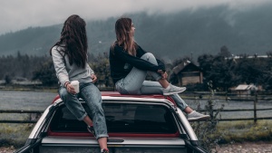 Two young adult women sitting on top of a car.