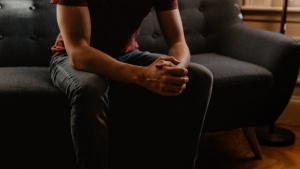 A young man sitting on a couch clasping his hands.