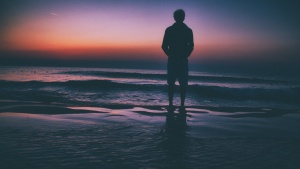 Um homem à beira de um lago ao pôr do sol.