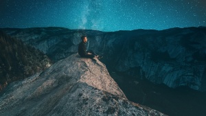 A young man sitting on a rock looking at the night sky.