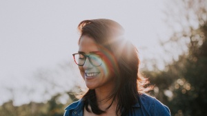 A young woman smiling with sun rays behind her head.