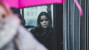 A woman looking out a window when it is raining.