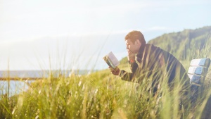 Man sitting in field studying Bible alone.